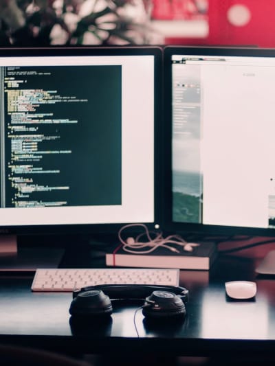 Coding work on a dual-monitor setup on a desk with headphones and cell phone.